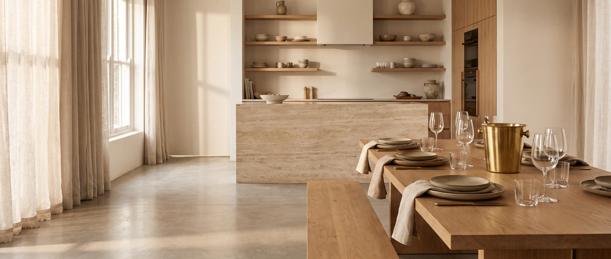 Oak dining table set with stoneware and glassware beside a modern kitchen